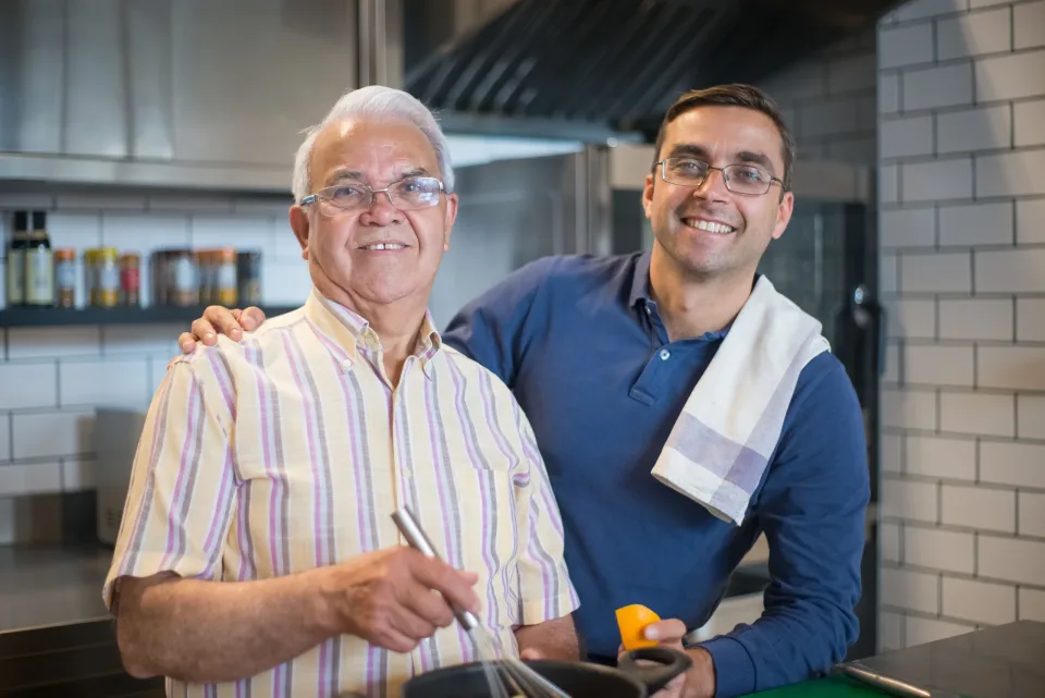 Older man and caregiver smiling together in a home kitchen