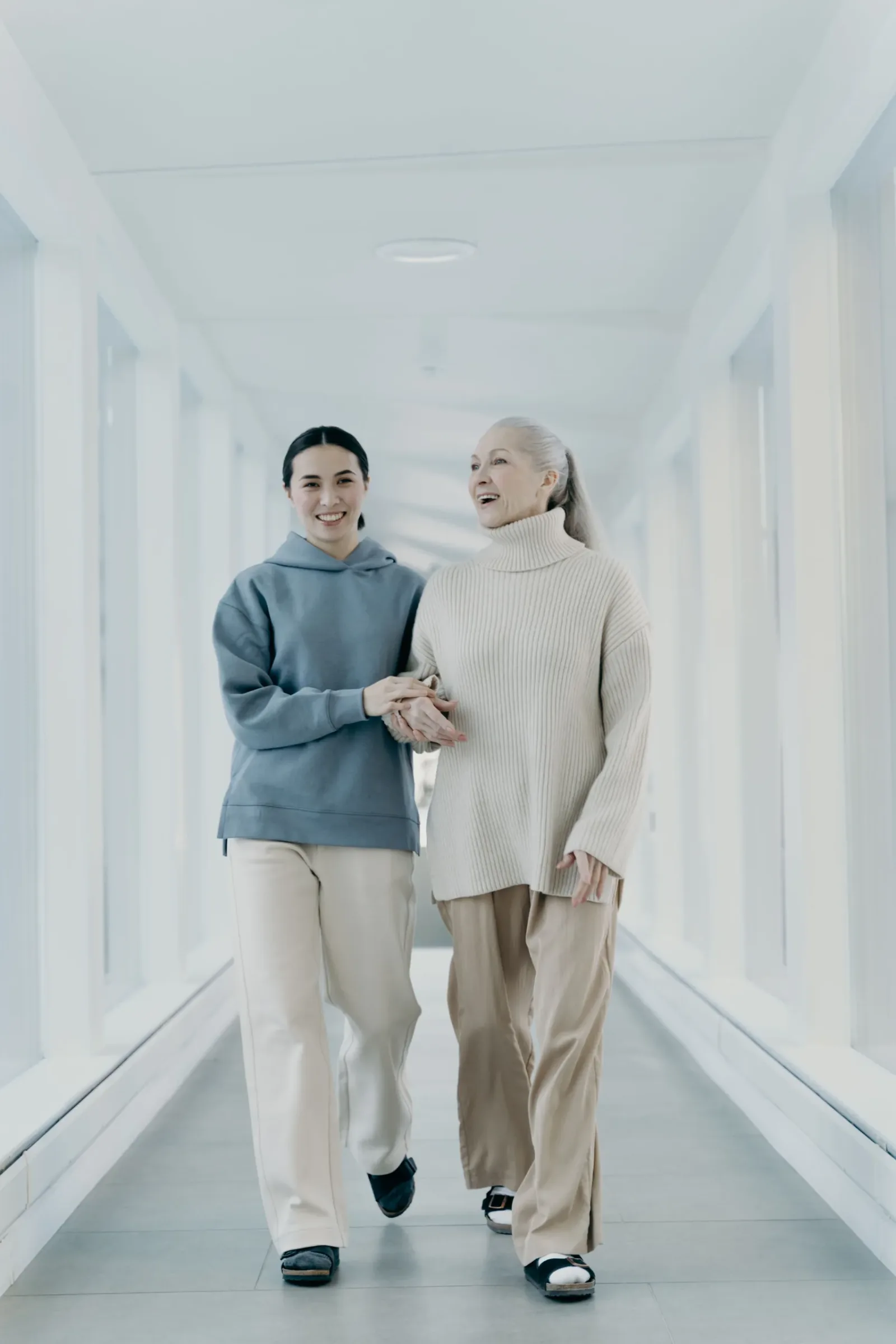 Caregiver walking beside an older woman in a bright hallway
