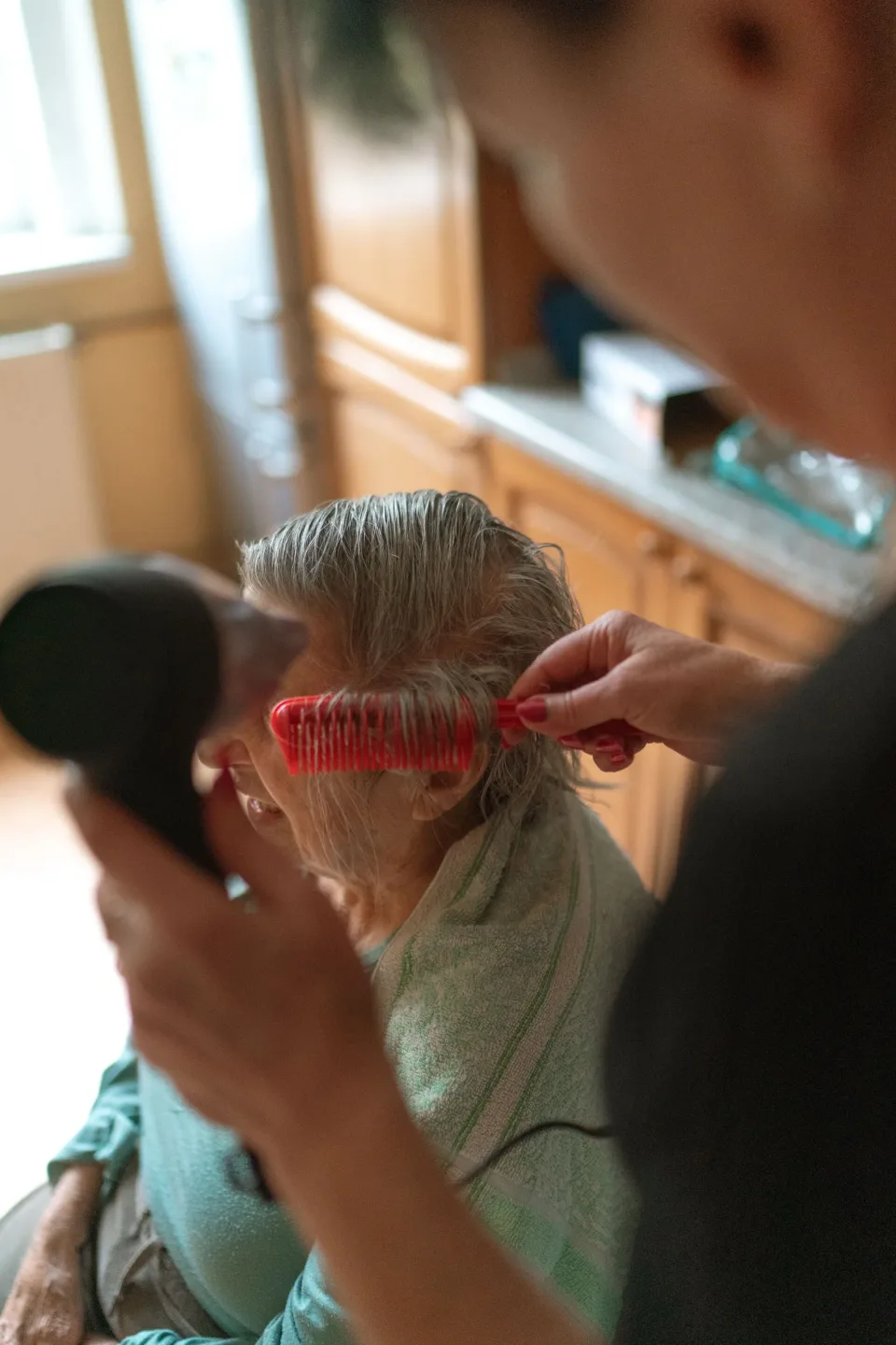 Caregiver gently brushing an older woman's hair at home