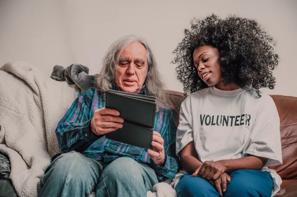 Volunteer helping an older man use a tablet at home
