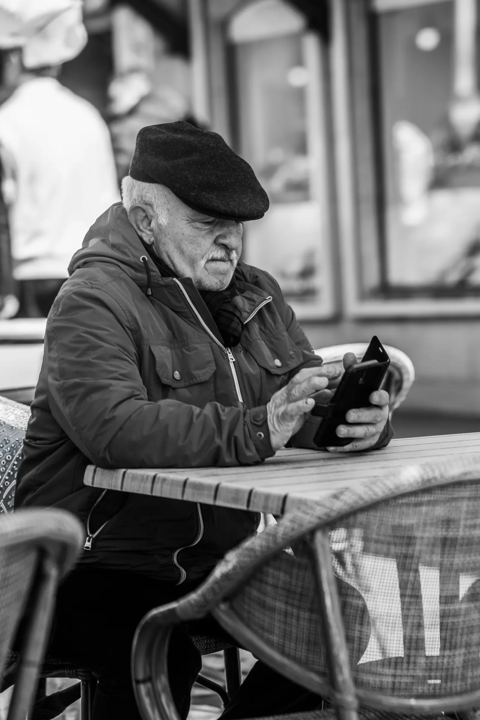 Older man using a smartphone while seated at an outdoor cafe