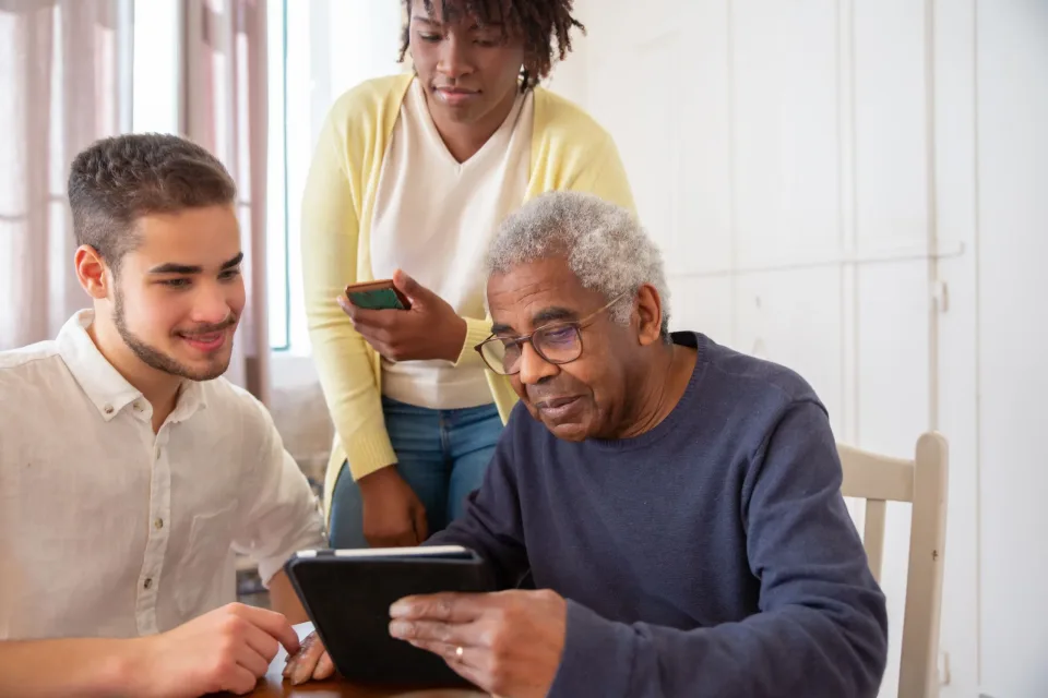 Family members helping an older man use a tablet at home