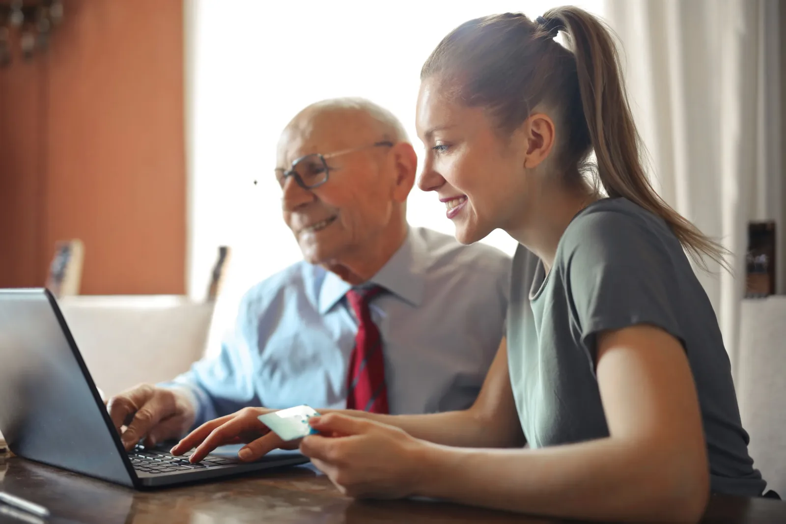 Caregiver helping an older man use a laptop at home