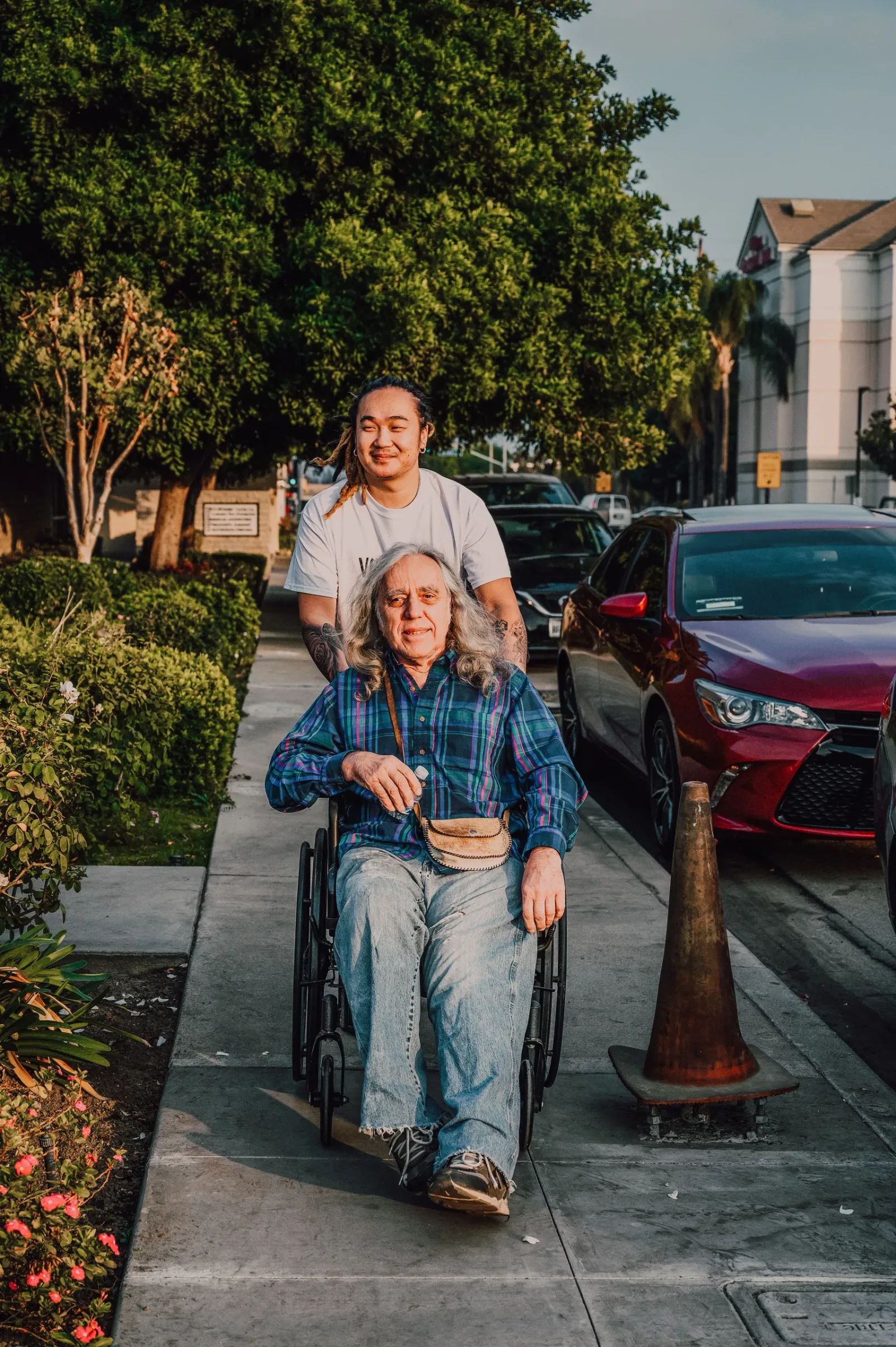 Caregiver pushing an older woman in a wheelchair along a neighborhood sidewalk