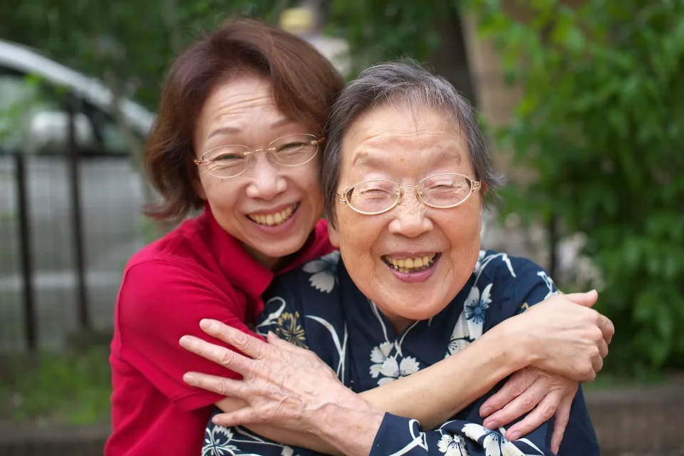 Two older women embracing and laughing together outdoors