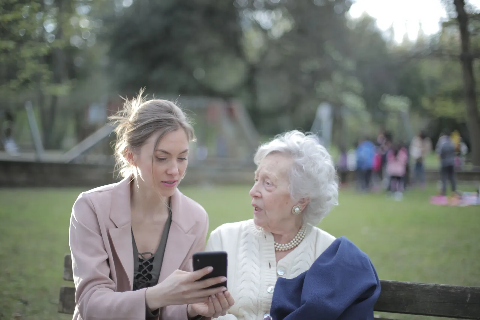 Companion showing an older woman something on a smartphone in a park